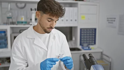 Foto op Canvas Arabian young man scientist, deeply concentrated in his analysis, looking at a sample in lab with focus, balancing research and safety with professionalism in science © Krakenimages.com