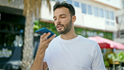 Young hispanic man sending voice message with smartphone at street