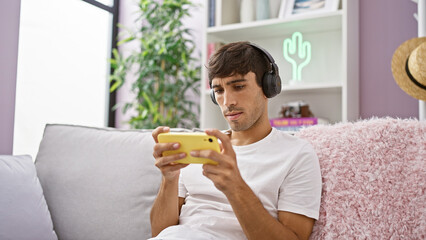 Young hispanic man playing video game sitting on sofa at home