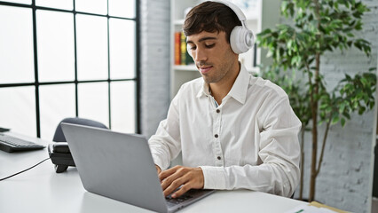 Young, focused hispanic business man at work in office, headphones on, immersed in laptop, bossing success!