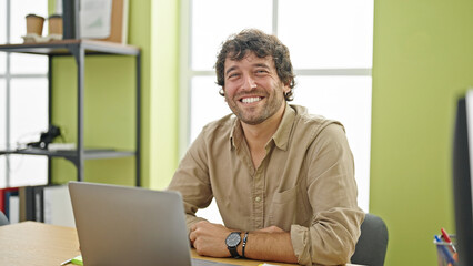 Fototapeta premium Young hispanic man business worker smiling confident sitting on table at office