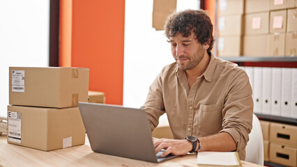 Young hispanic man ecommerce business worker typing on computer smiling at office