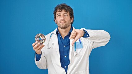 Young hispanic man nutritionist holding doughnut doing thumb down gesture over isolated blue background