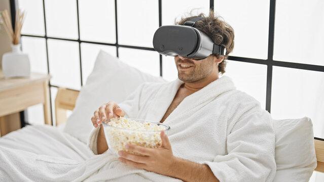 Young hispanic man watching movie using virtual reality glasses at bedroom