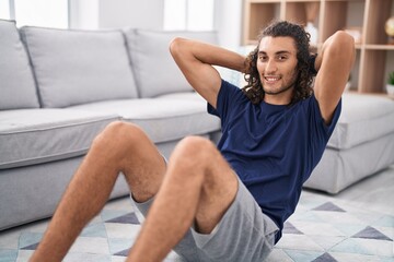 Young hispanic man smiling confident training abs exercise at home