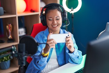 Young chinese woman streamer playing video game using smartphone at gaming room