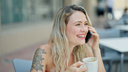 Young blonde woman talking on smartphone drinking coffee at coffee shop terrace