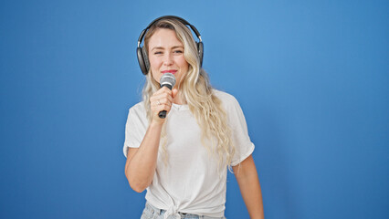 Young blonde woman listening to music singing song over isolated blue background