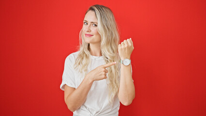 Young blonde woman smiling confident pointing to watch over isolated red background