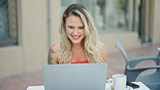 Young blonde woman using laptop sitting on table at coffee shop terrace