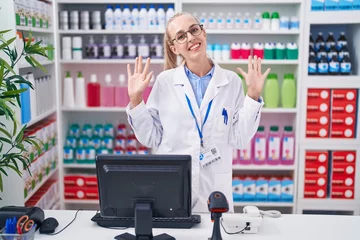 Fotobehang Young caucasian woman working at pharmacy drugstore showing and pointing up with fingers number ten while smiling confident and happy. © Krakenimages.com