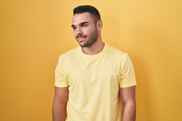 Obraz premium Young hispanic man standing over yellow background smiling looking to the side and staring away thinking.