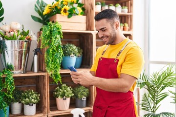 Young hispanic man florist smiling confident using smartphone at florist