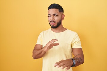 Young hispanic man standing over yellow background disgusted expression, displeased and fearful...