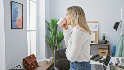 Caucasian blonde woman drinking coffee in a modern office, evoking a professional, relaxed...