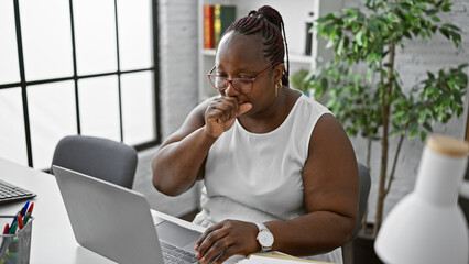 Braided african american business woman, relaxed yet focused, working diligently amidst coughing...
