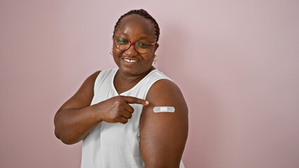 Confident african american woman smiling joyfully, pointing at band aid on arm over an isolated...