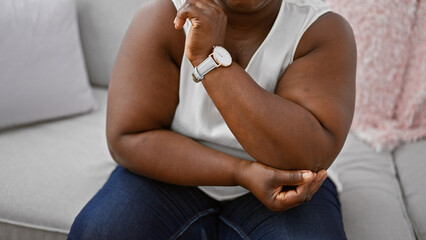 Unhappy african american woman, relaxing on comfy sofa at home, bravely bearing pain from elbow...