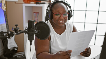 Positive plus-sized african american woman with braids, smiling while professionally reading latest...