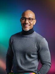 Obraz premium The image features a smiling man with glasses and a grey turtleneck, standing in front of a colorful background.