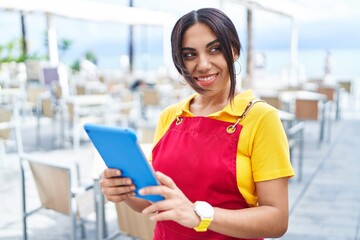 Young beautiful arab woman waitress smiling confident using touchpad at coffee shop terrace