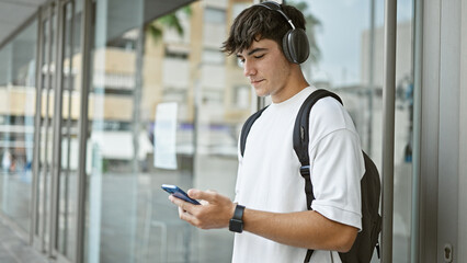 Cool young hispanic university student immersed in music, tapping on smartphone screen under campus...