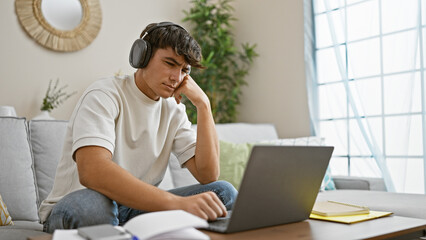 Engrossed young hispanic male student chilling at home, sitting on comfy sofa, focused on studying...