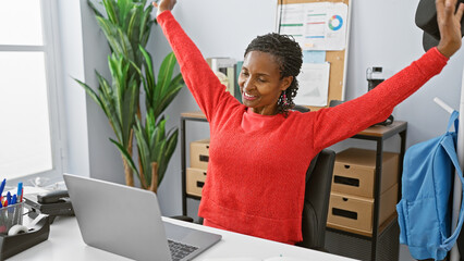 A joyful african american woman stretching in a modern office setting, portraying workplace...