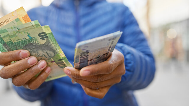 A woman holds south african rand on a city street, exemplifying finance, economy, shopping, or travel in an urban setting.