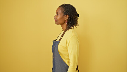 Profile of a mature african woman wearing a yellow sweater and denim apron against an isolated...