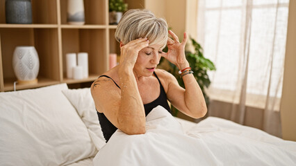 Mature woman with grey hair looking stressed in a bedroom setting, depicting health or mental well-being concepts.