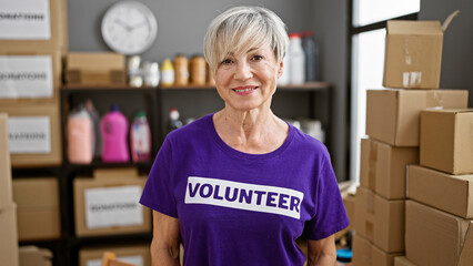 Mature woman volunteer smiles in warehouse surrounded by donations and boxes.