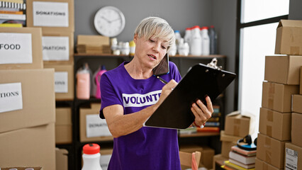 Hispanic woman multitasking on phone and clipboard in a busy donation center warehouse interior