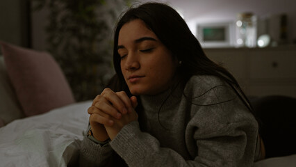 A thoughtful young hispanic woman rests peacefully in a dimly lit room at night, exuding...