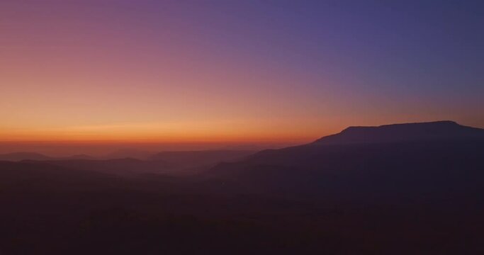 Aerial view A breathtaking sunset paints the sky with vibrant hues of orange and red, .casting a warm glow over the majestic mountains in a tranquil evening landscape.colorful layer of mountain range.