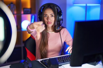 Young hispanic woman playing video games looking unhappy and angry showing rejection and negative with thumbs down gesture. bad expression.