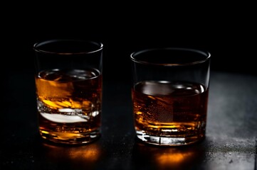 Two glasses of whiskey with ice on a black background, selective focus