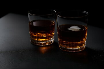 Two glasses of whiskey with ice on a black background, selective focus