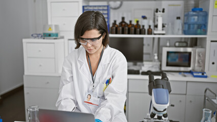 Dedicated young hispanic woman scientist, focused at her laptop in the lab, part of a new wave of...
