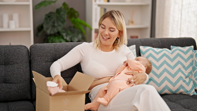 Mother and daughter holding baby clothes of package sitting together at home
