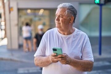 Middle age grey-haired man smiling confident using smartphone at street