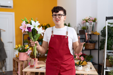 Young non binary man working at florist shop showing smartphone screen angry and mad screaming frustrated and furious, shouting with anger. rage and aggressive concept.