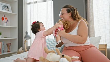 Confident mother and cheerful daughter enjoying playtime with toys, sitting on a comfy bed in a...
