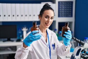 Young caucasian woman scientist holding bottles at laboratory