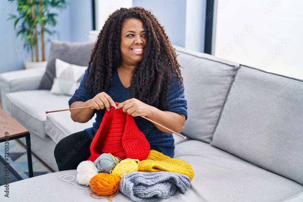 Poster african american woman sitting on sofa sewing handmade clothes at home