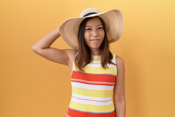 Middle age chinese woman wearing summer hat over yellow background confuse and wondering about...