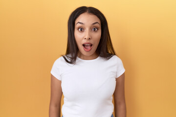 Young arab woman wearing casual white t shirt over yellow background afraid and shocked with surprise and amazed expression, fear and excited face.