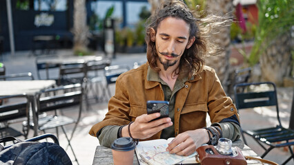 Fototapeta premium Young hispanic man tourist using smartphone sitting on table at coffee shop terrace