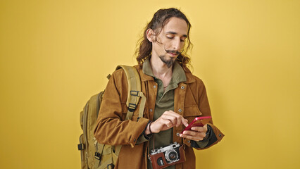 Young hispanic man tourist using smartphone over isolated yellow background