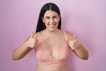 Young hispanic woman wearing pink bra success sign doing positive gesture with hand, thumbs up smiling and happy. cheerful expression and winner gesture.